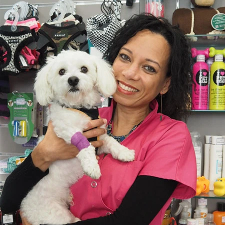 Auxiliaire vétérinaire souriante en blouse rose tenant un petit chien blanc dans une animalerie ou clinique.